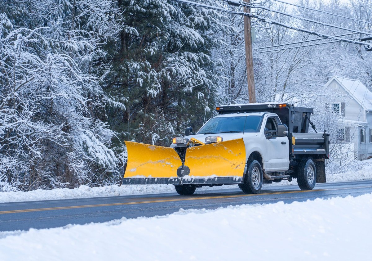 Professional truck with snow plow clearing residential driveway